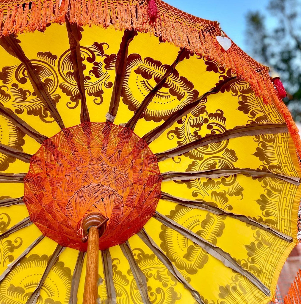 Luxury Arabella Parasol featuring golden patterns on yellow canvas with handcrafted wood and brass accents.